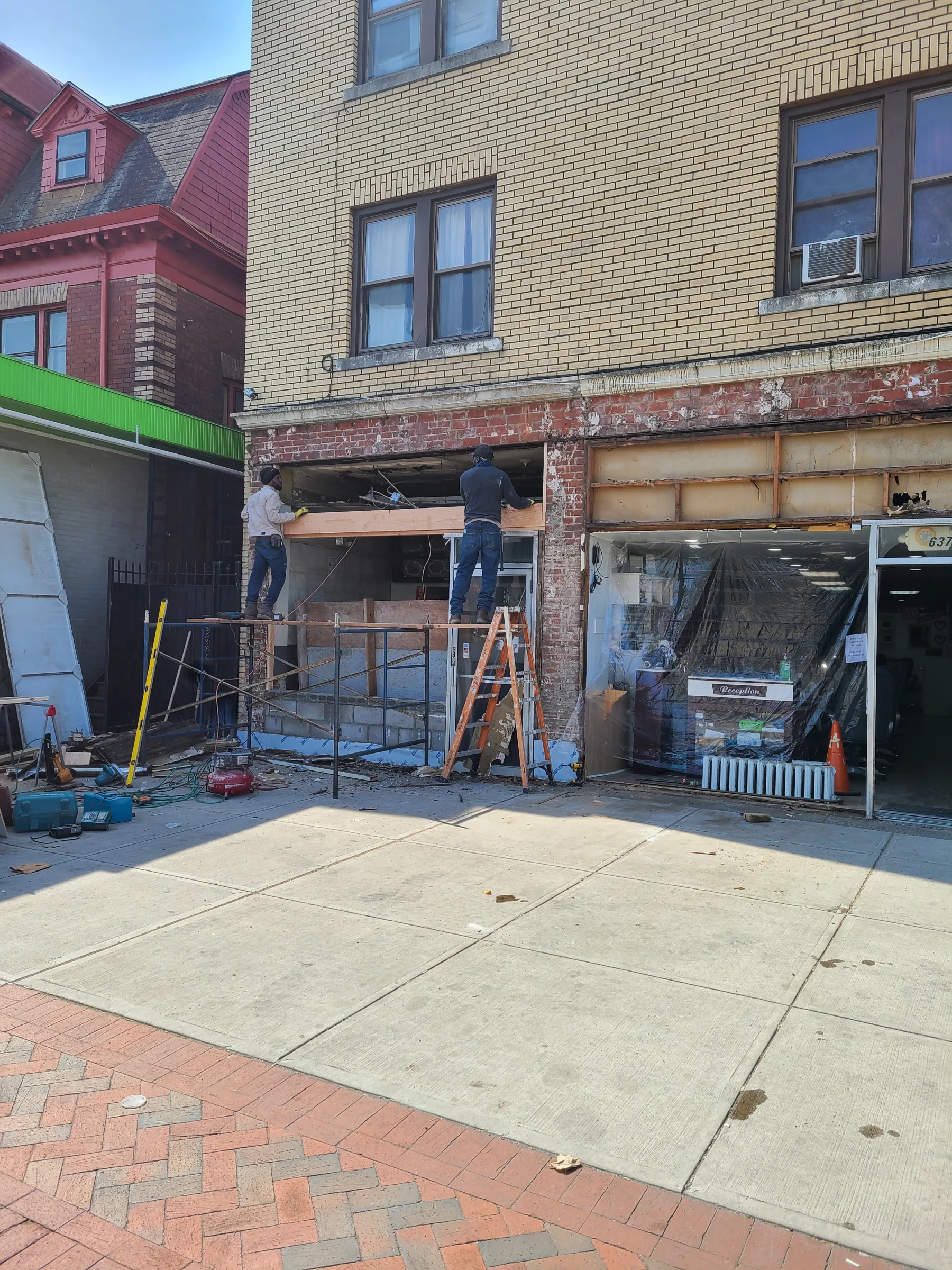 Workers rebuild the storefront bays with the framing, masonry, and construction access fully exposed.