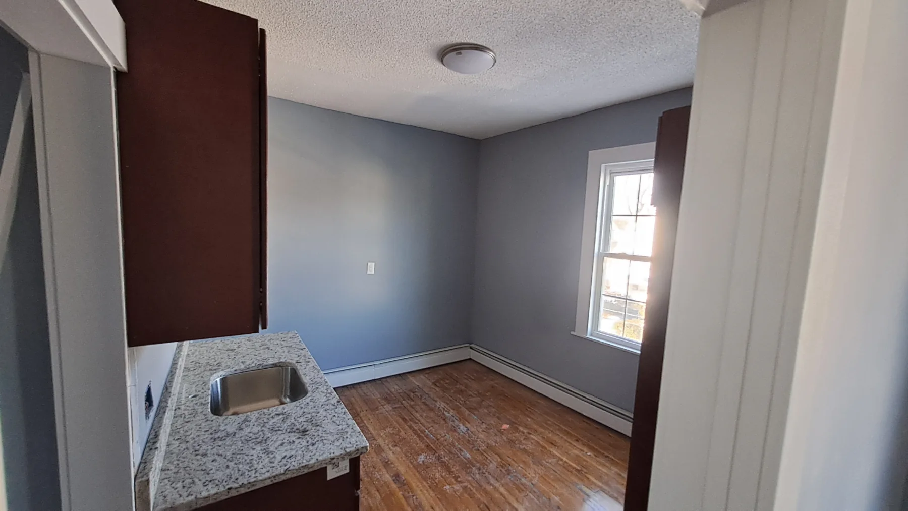 A renovated kitchenette shows new counters, cabinetry, flooring, paint, and restored natural light.