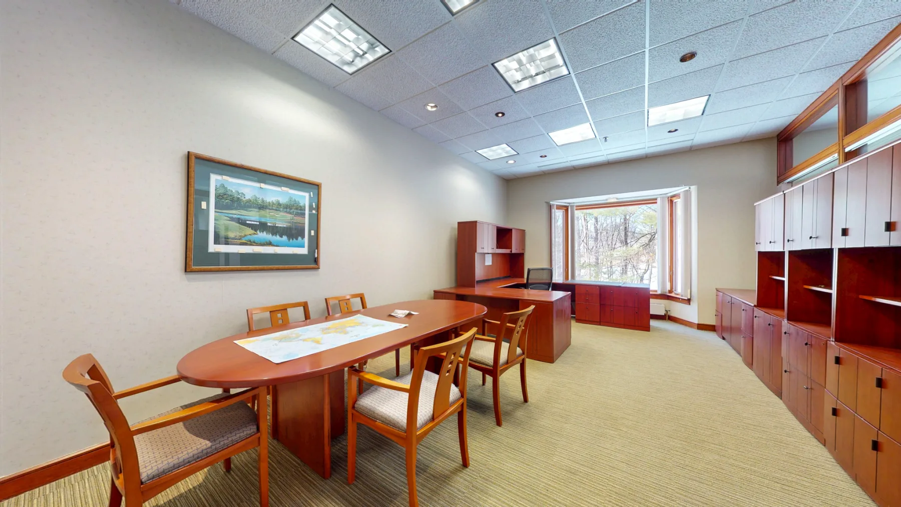 The conference room combines a full meeting table, perimeter storage, and broad wooded views.