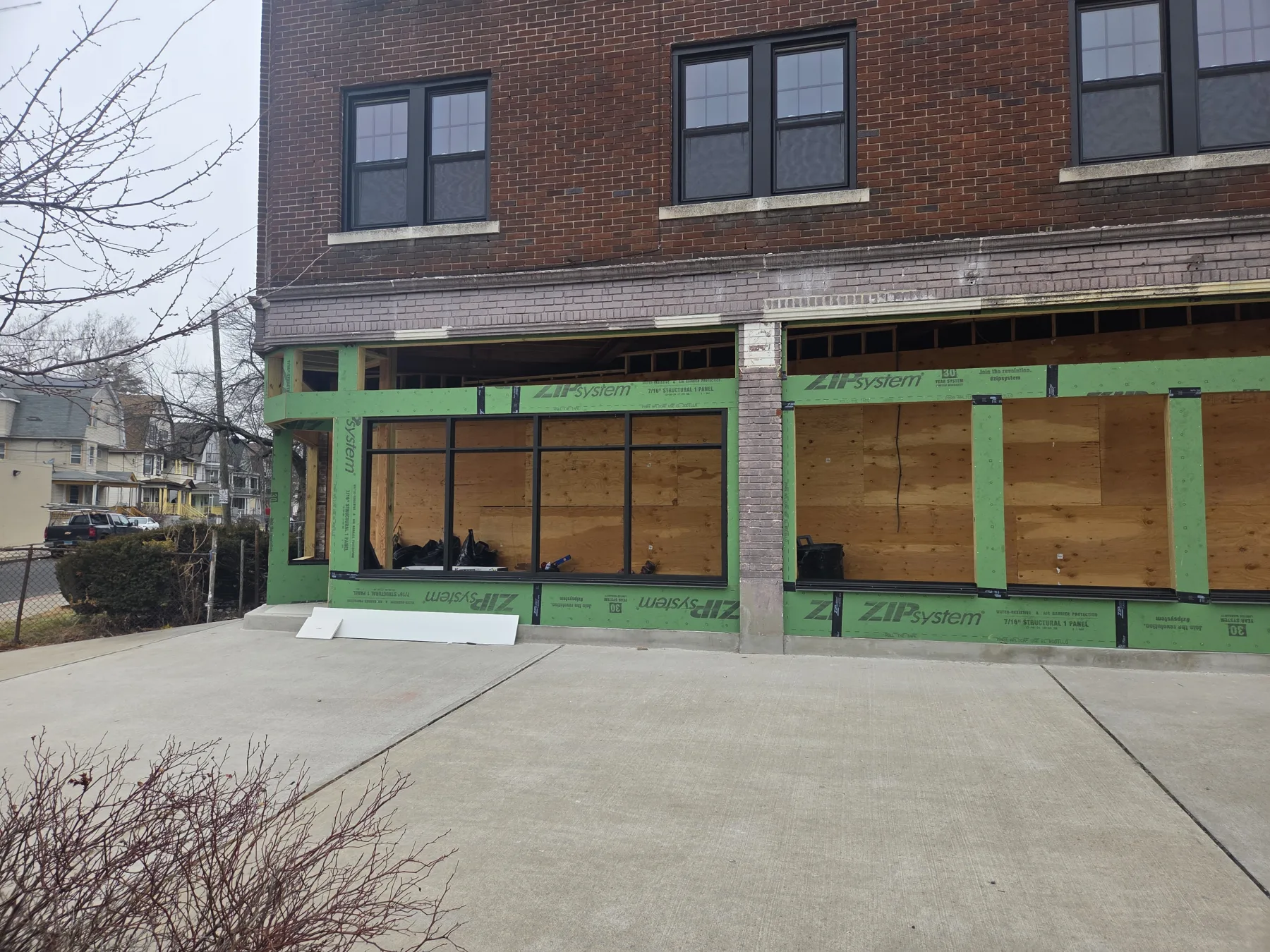 Green exterior sheathing and new black storefront frames mark visible progress toward a more open commercial frontage.