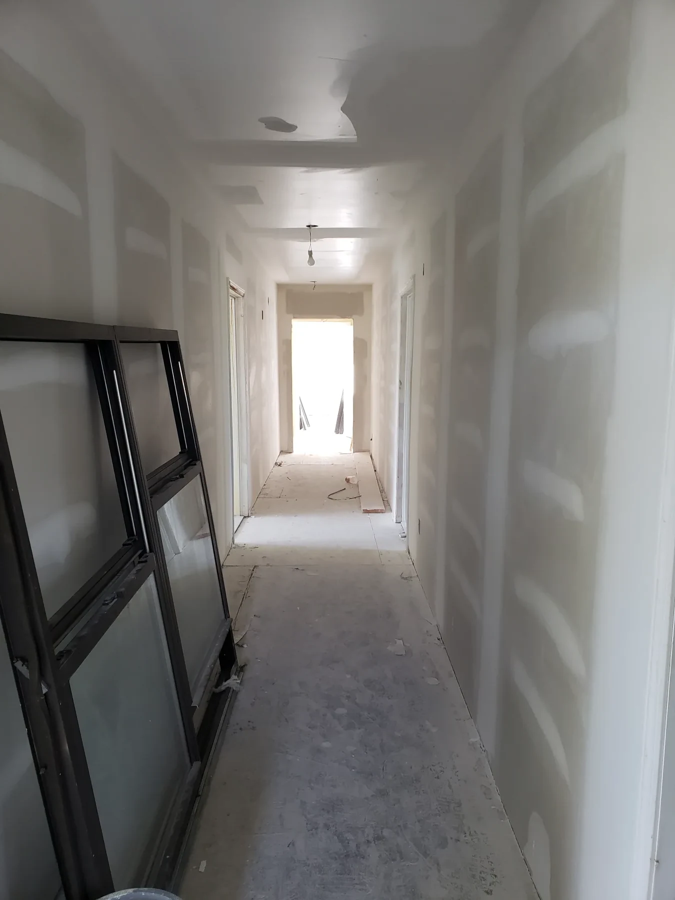 A residential corridor is rebuilt with new drywall while floor and finish work remain underway.