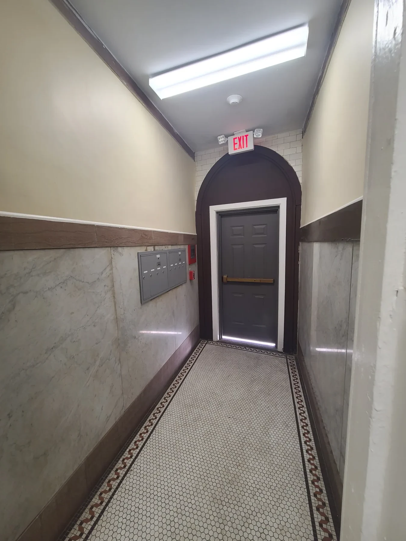 The restored common entry preserves the patterned floor and arched doorway while renewing lighting and finishes.