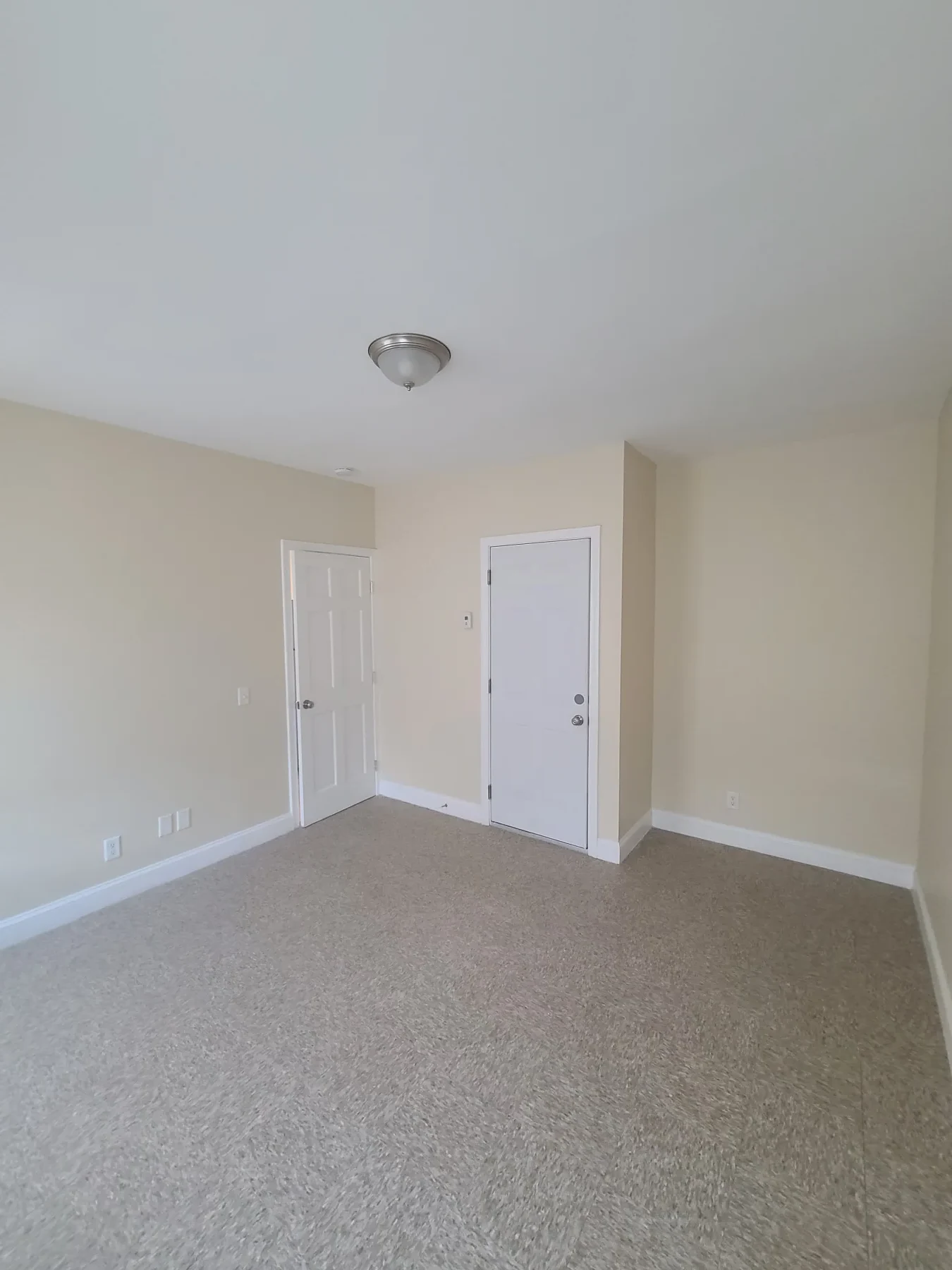 A finished bedroom shows new carpet, paint, trim, doors, and lighting.