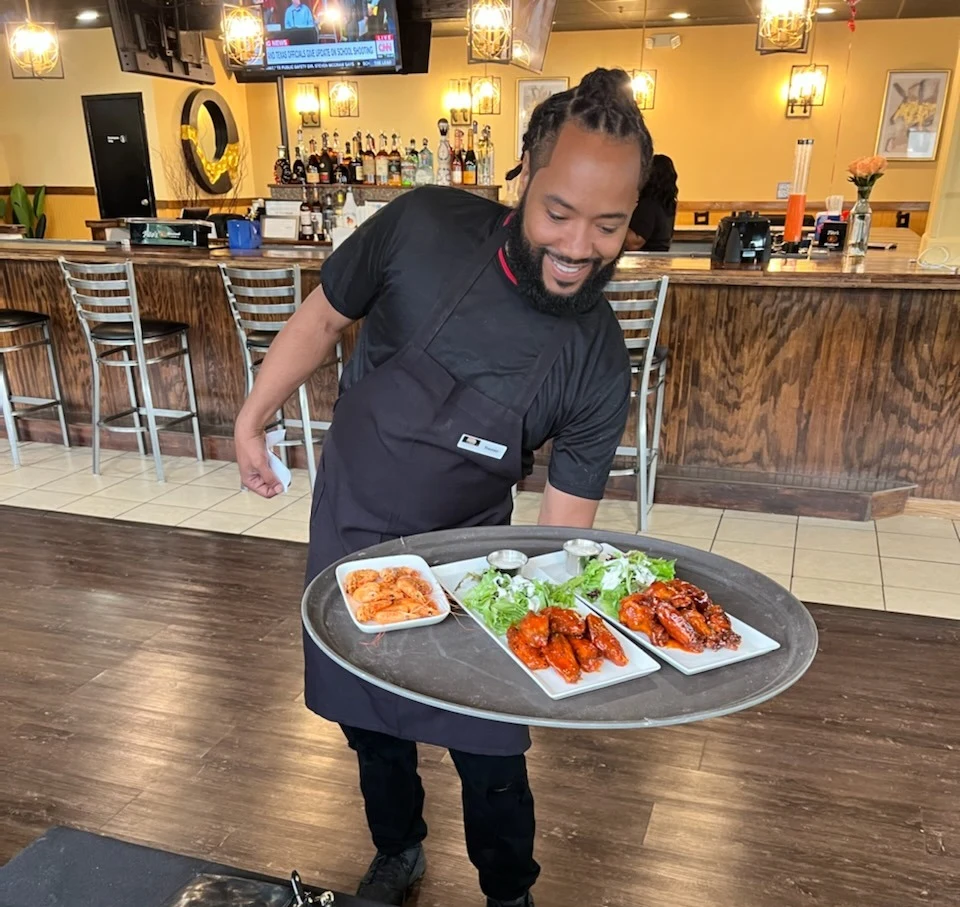 A smiling member of the Fish N Tingz team serving a tray of food
