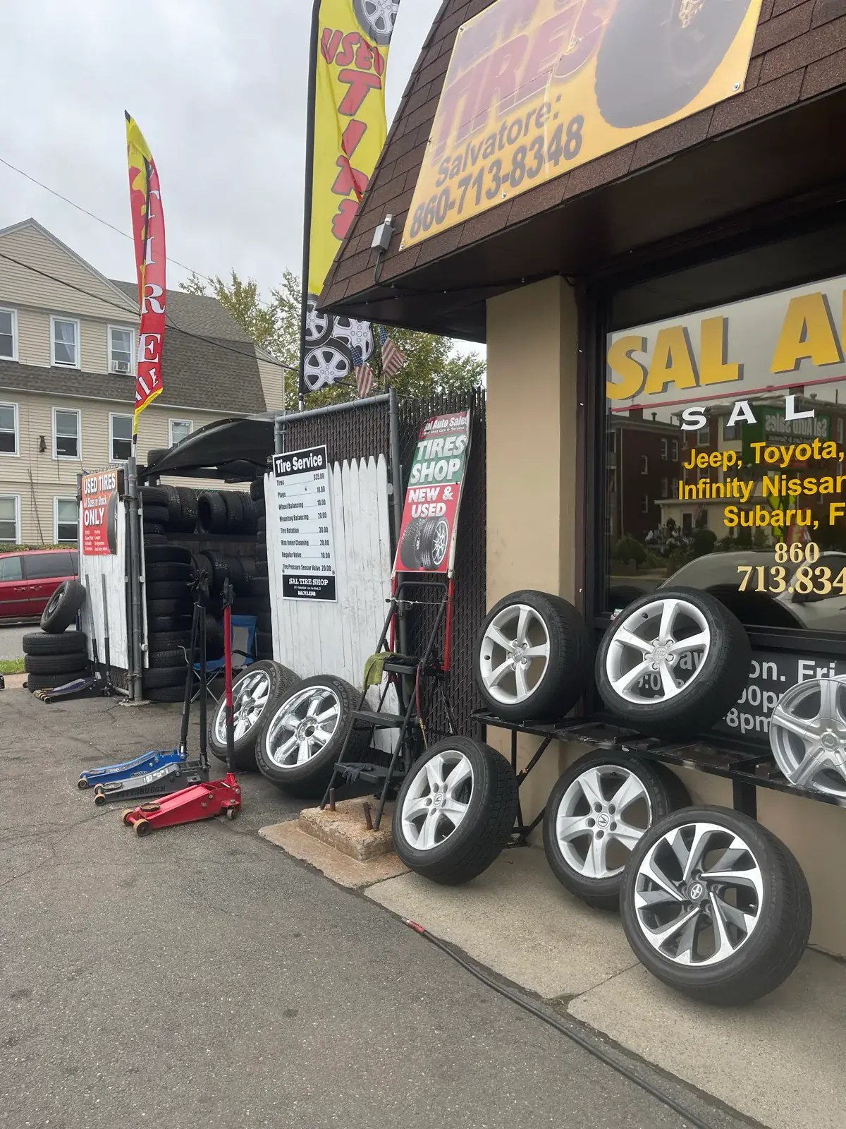 Tires and silver alloy wheels outside Sal’s Tire Shop, beside the posted service board